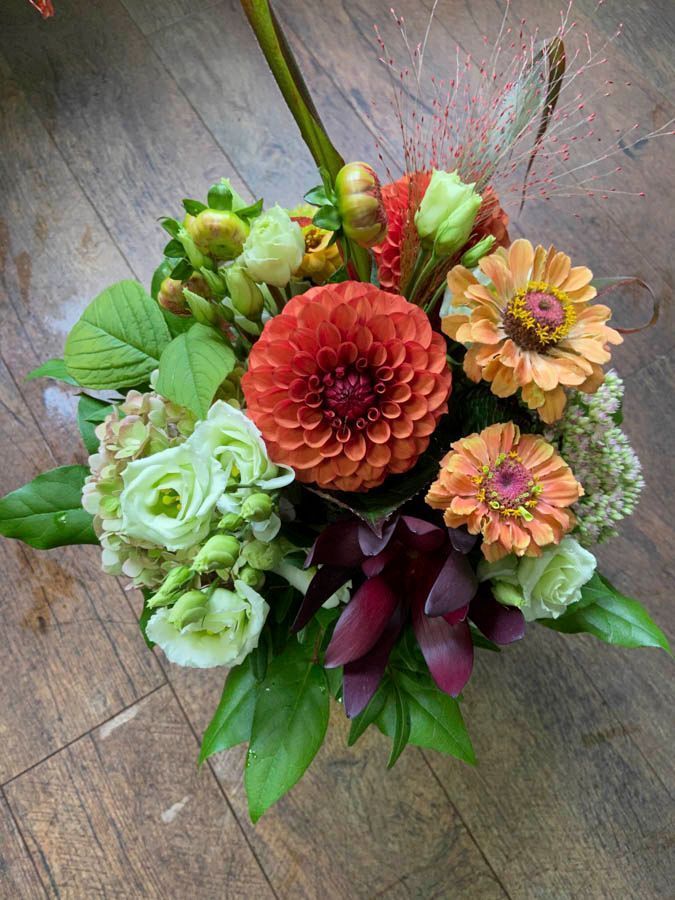 Gemischter Blumenstrauß mit orangefarbenen Dahlien, hellgrünen Rosen und rosa Blüten auf einer Holzoberfläche