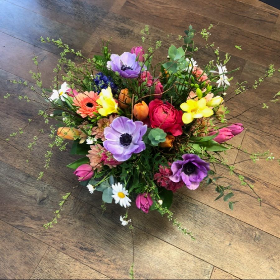 Ein bunter, gemischter Wildblumenstrauß auf einem Holzboden mit lila, rosa, gelben und weißen Blüten.