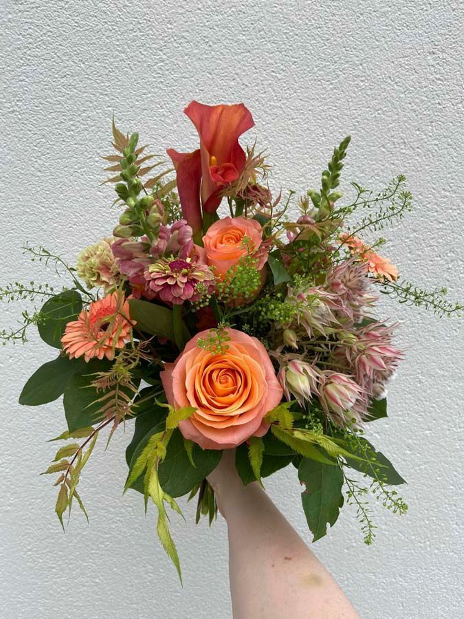 Handstrauß aus orangefarbenen und rosafarbenen Blumen mit Grün vor hellem Hintergrund