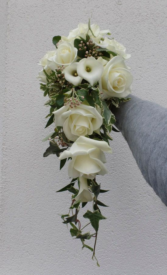 Ein weißer Brautstrauß mit Rosen und Calla-Lilien, akzentuiert mit Grün, vor einer grauen Wand