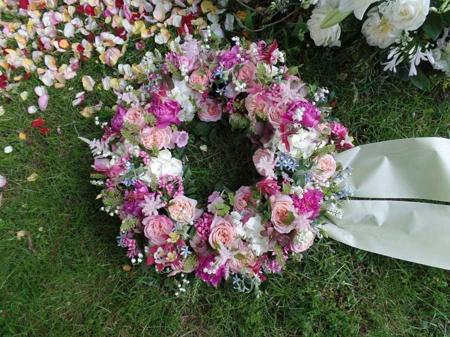 Rosa-weißer Blumenkranz auf Gras mit weißem Schleifenband