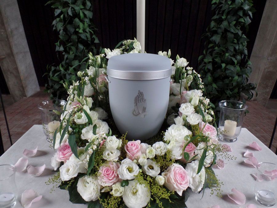 Eine mit weißen und rosa Blumen umgebene Urne auf einem Gedenktisch
