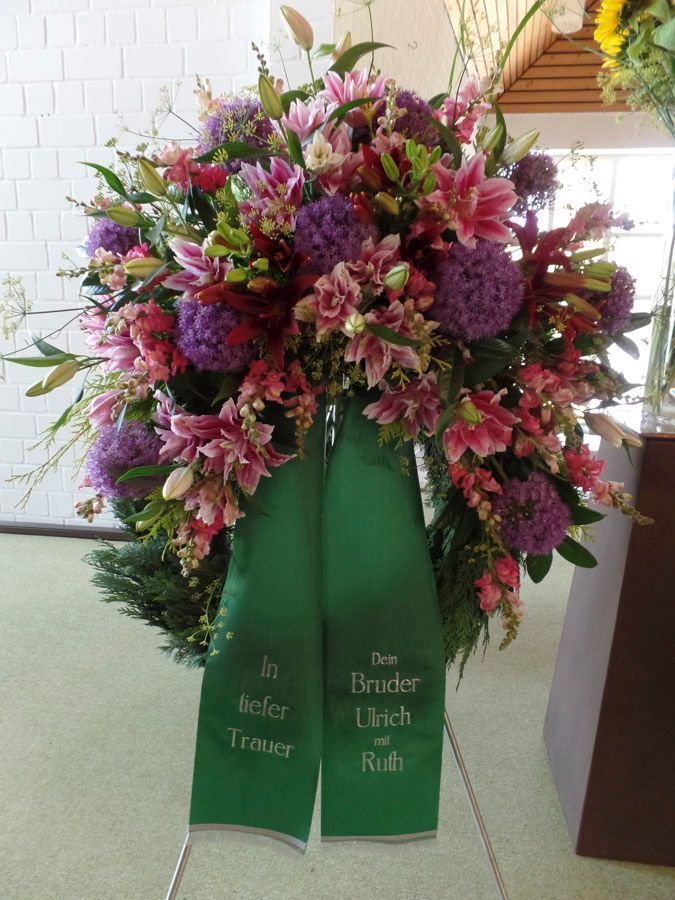 Großer rosa-lila Blumenkranz auf einem grünen Trauerständer mit Bändern