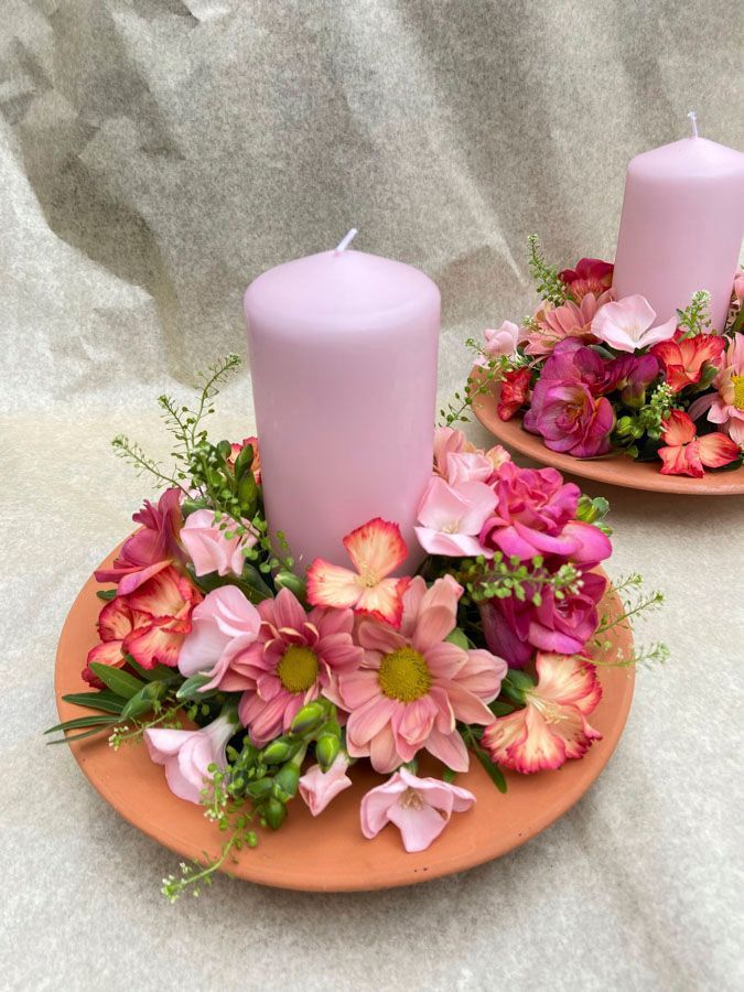 Ein rosa-weißes Blumen-Kerzenarrangement auf einem Terrakotta-Tablett mit Grünzeug und zwei Lavendelkerzen.