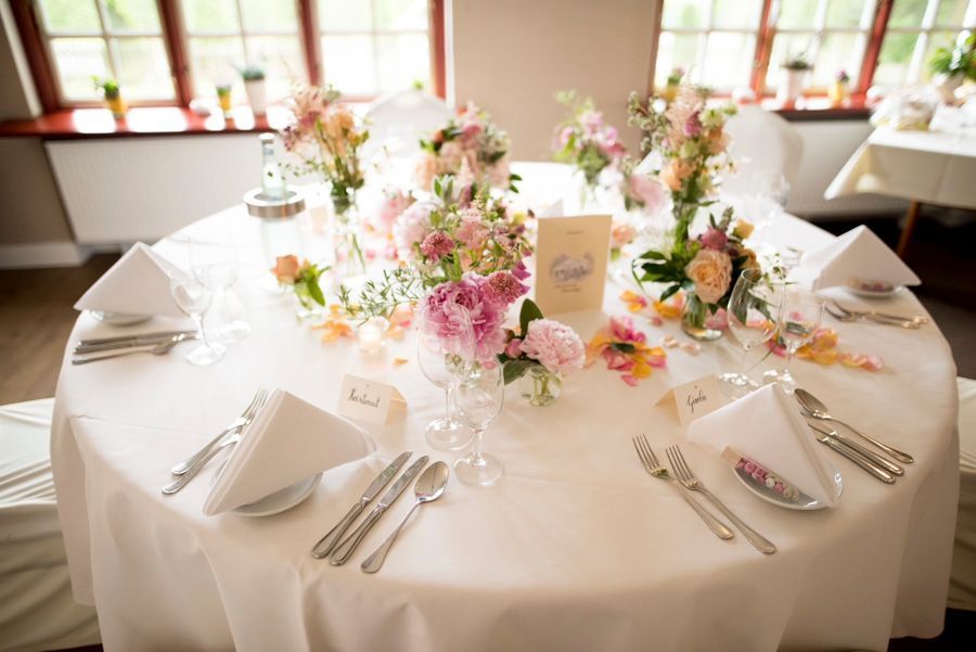 Runder Festtisch, gedeckt mit weißer Tischwäsche, Blumengestecken, gefalteten Servietten und Silberbesteck in einem hellen Esszimmer