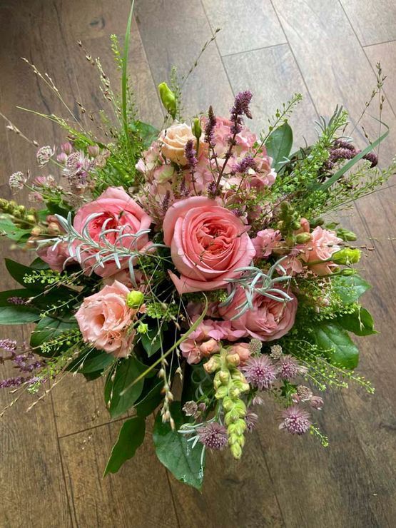 Rosa- und pfirsichfarbener Rosenstrauß mit Grünzeug und zarten Füllblumen auf rustikalem Untergrund