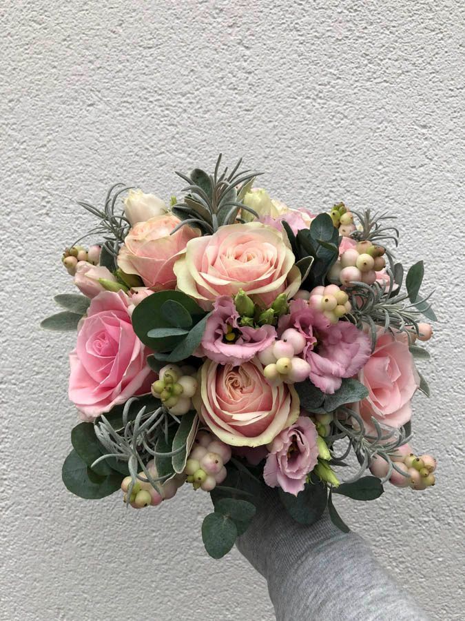 Ein pastellrosa-cremefarbener Blumenstrauß mit Grünzeug, vor einer schlichten Wand.