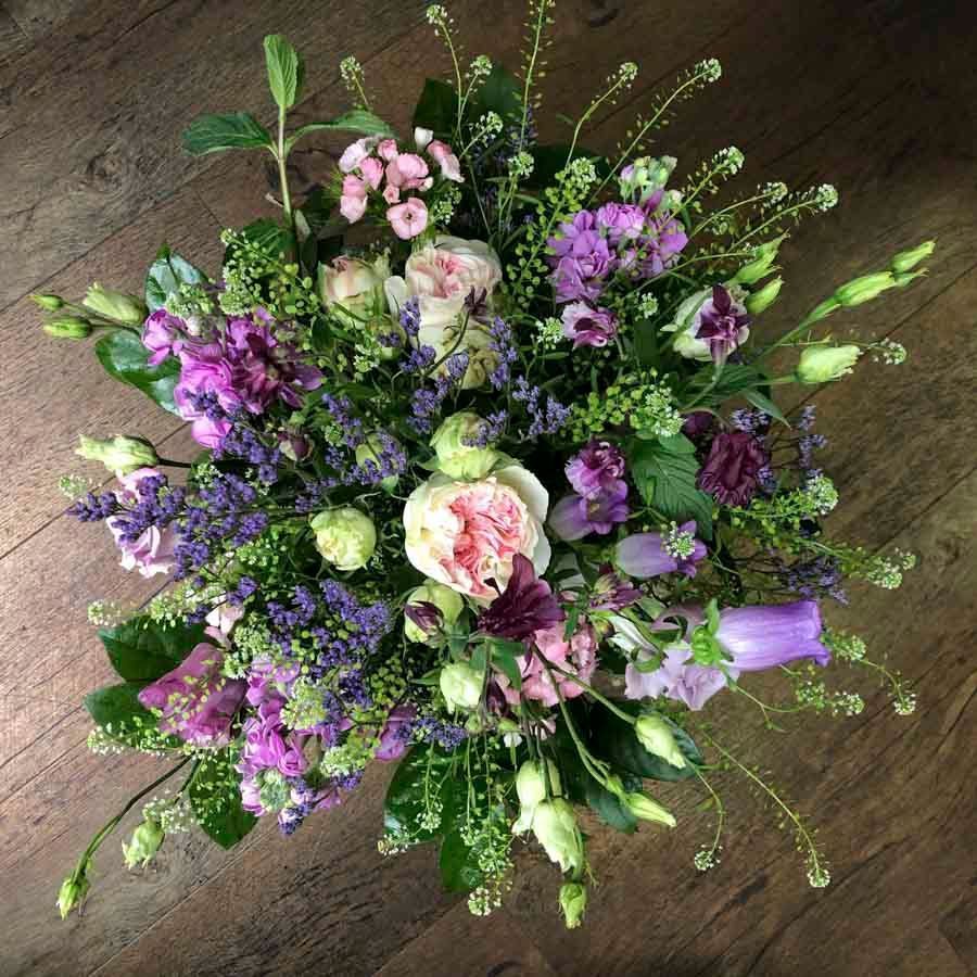 Ein pastellrosa, lila und weißes Blumenstrauß auf einem Holzboden
