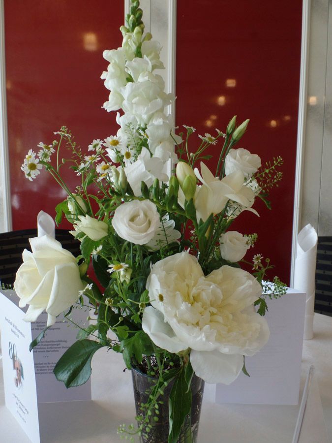 Weißes Blumenarrangement in einer Glasvase auf einem Tisch vor rotem Hintergrund