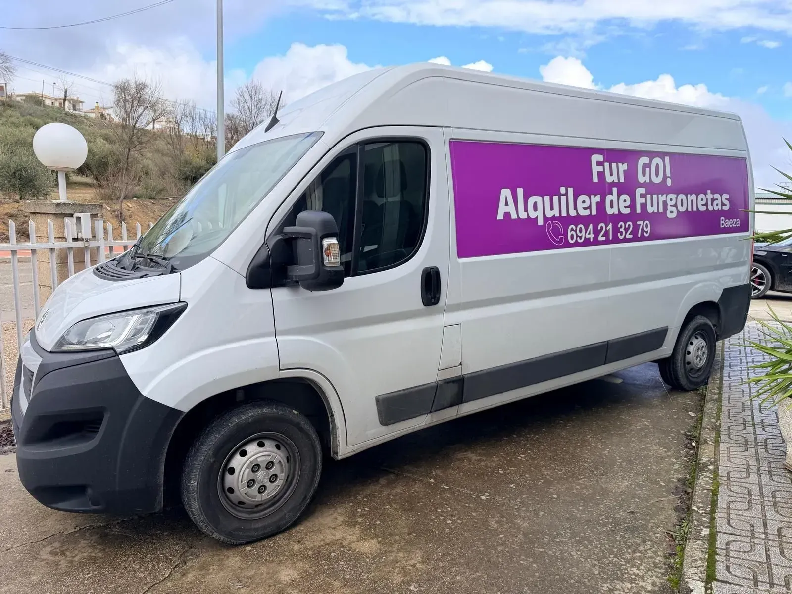Furgoneta blanca de carga con letrero morado de alquiler “For GO! Alquiler de Furgonetas” estacionada al aire libre.