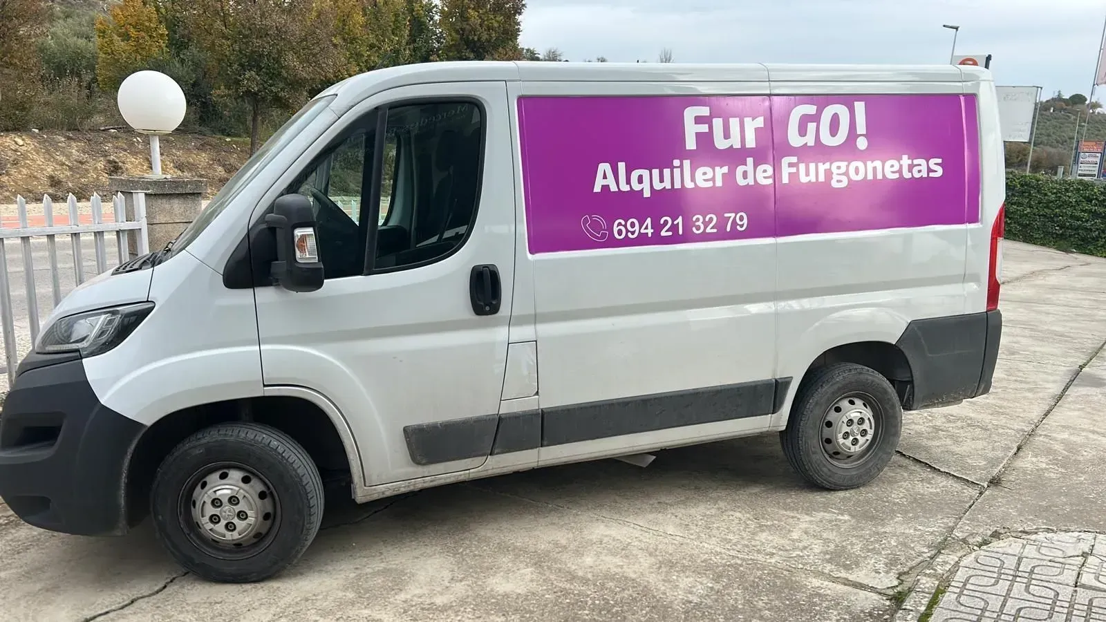Furgoneta blanca de carga con un letrero rosa de “Fur GO! Alquiler de Furgonetas” estacionada al aire libre.