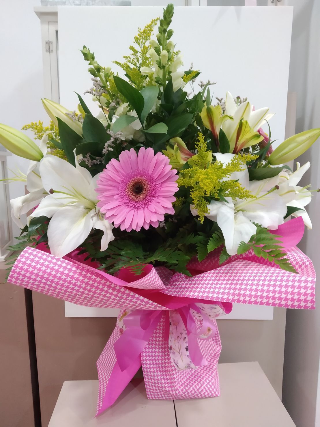 Un ramo de flores rosas y blancas envuelto en papel rosa.