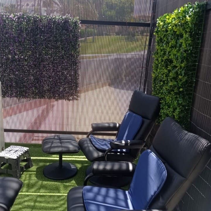 Un patio con sillas y otomanas y una valla.