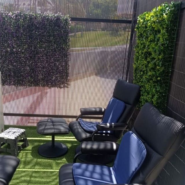 Un patio con sillas y otomanas y una valla.