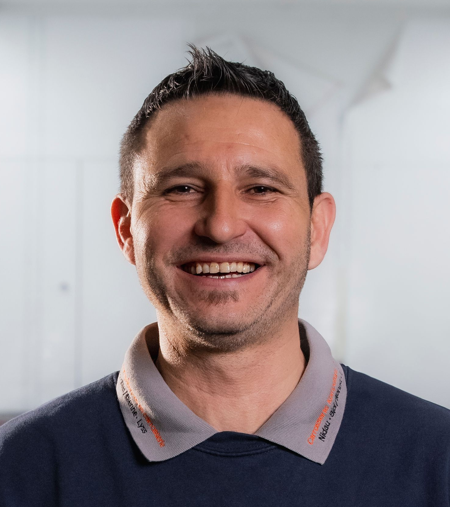 Ein Mann in einem dunkelblauen Hemd lächelt in einer Werkstatt in die Kamera.