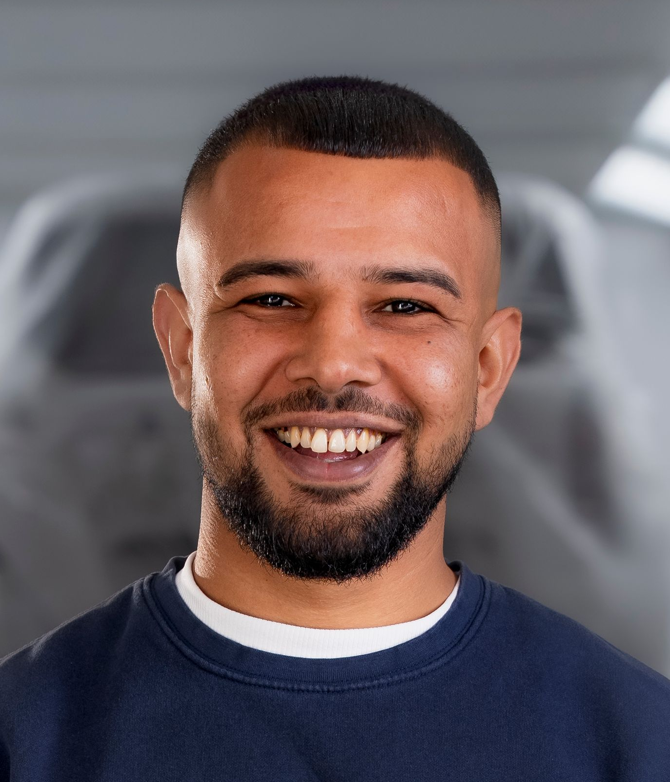 Mann mit ergrauendem Haar und Bart, lächelnd, trägt ein blaues Sweatshirt mit Text, drinnen.