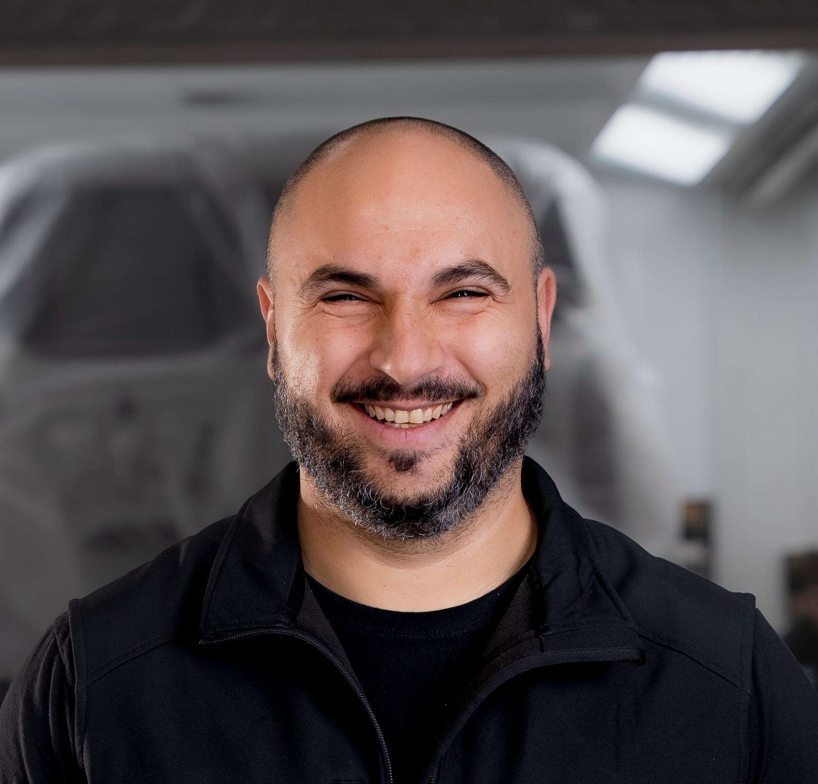 Mann mit ergrauendem Haar und Bart, lächelnd, trägt ein blaues Sweatshirt mit Text, drinnen.