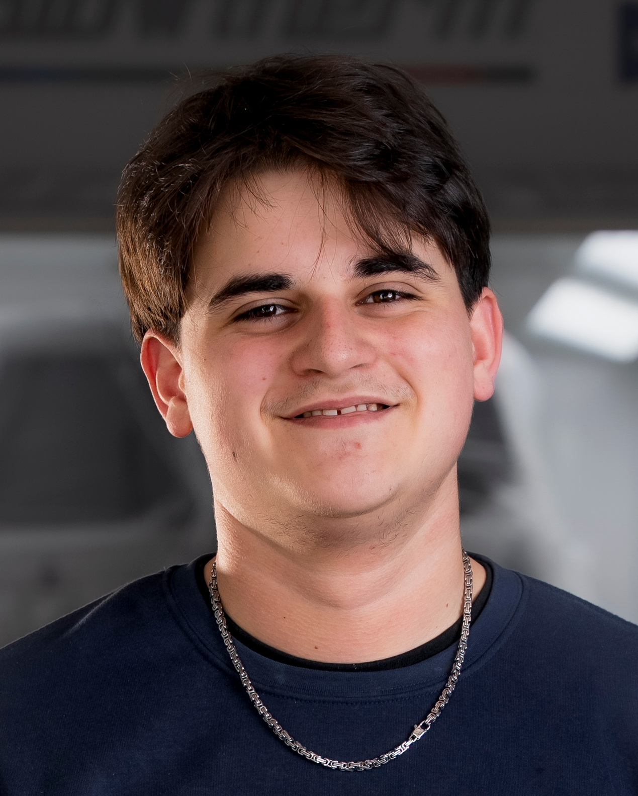 Mann mit ergrauendem Haar und Bart, lächelnd, trägt ein blaues Sweatshirt mit Text, drinnen.