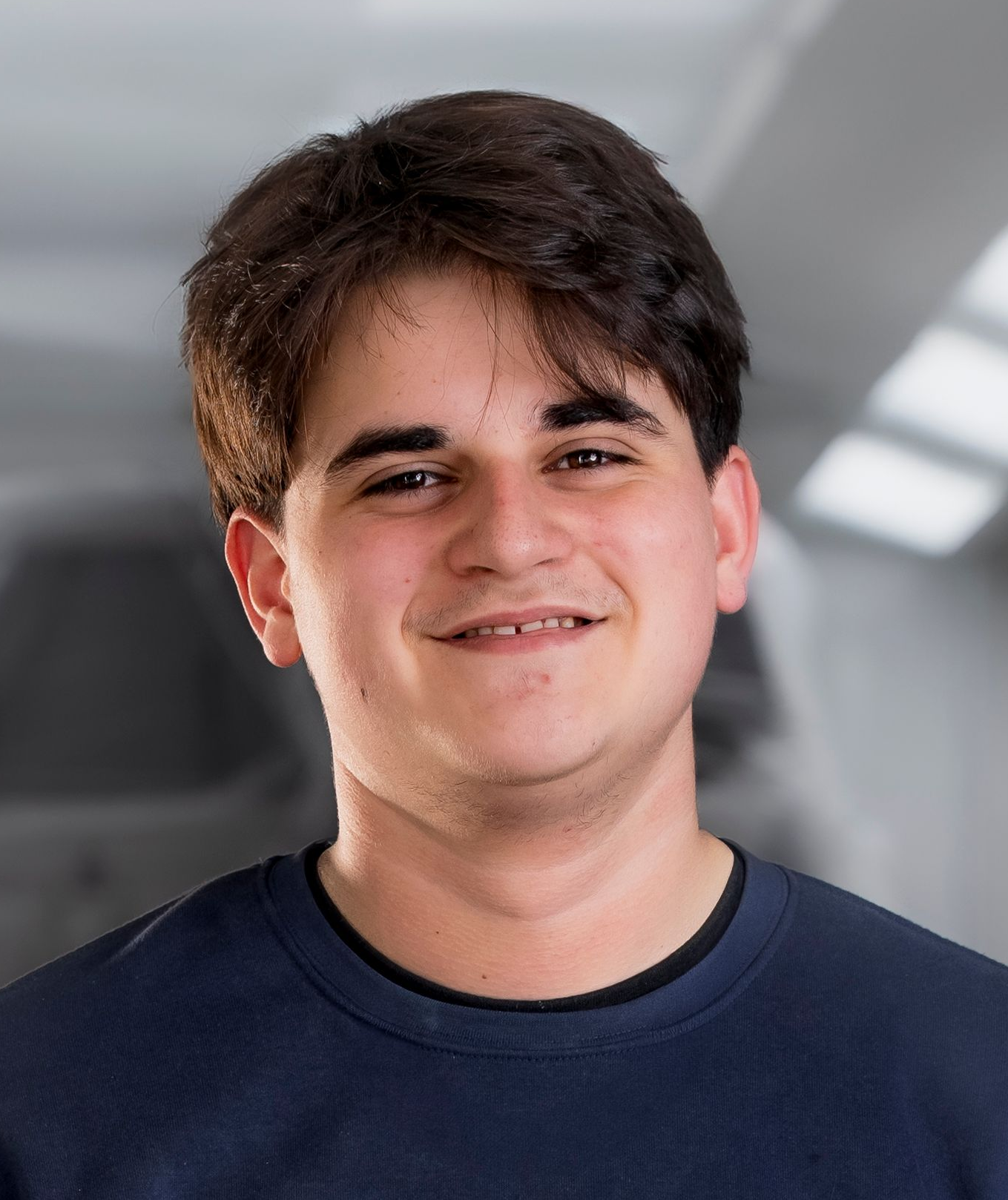 Mann mit ergrauendem Haar und Bart, lächelnd, trägt ein blaues Sweatshirt mit Text, drinnen.