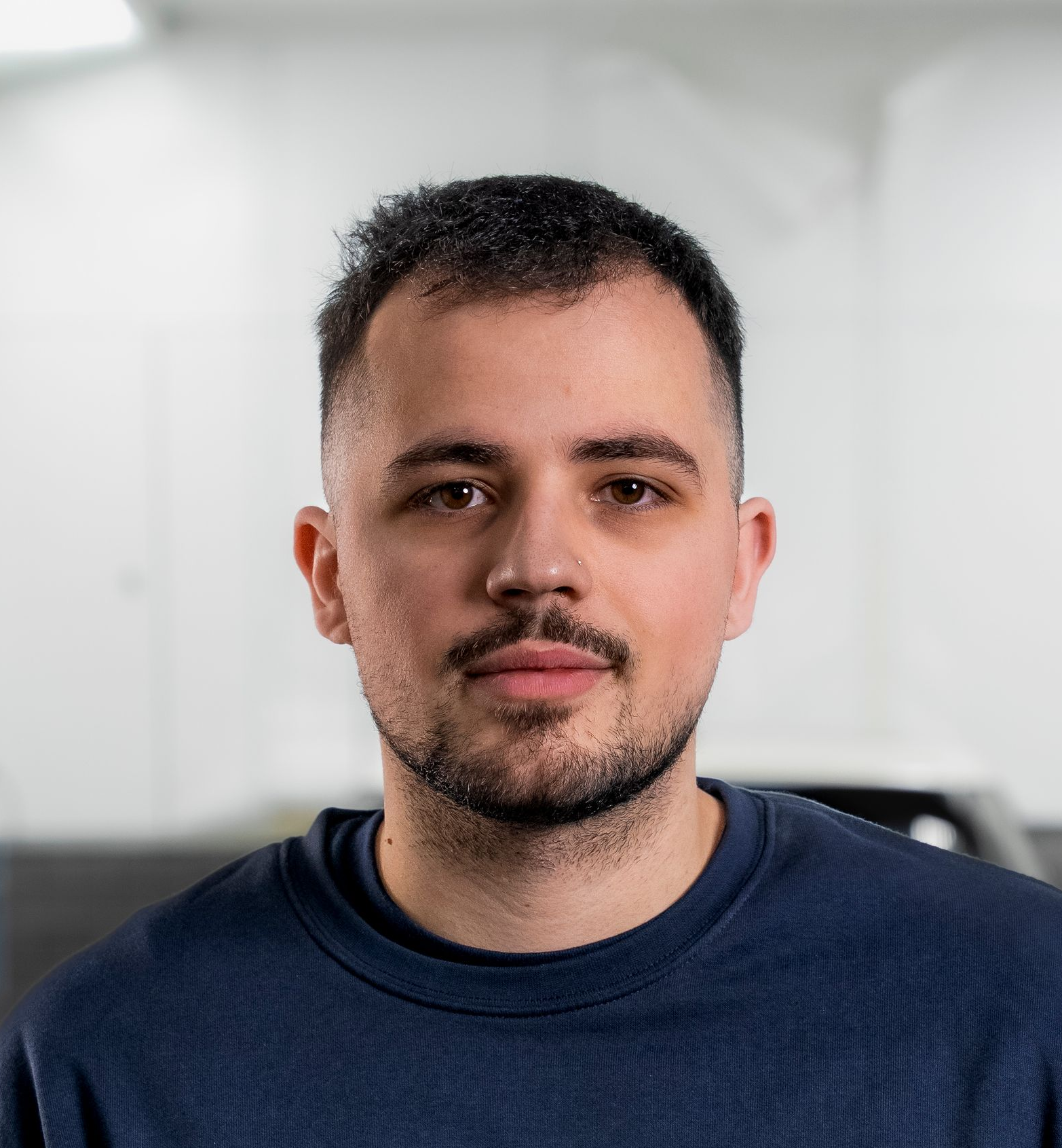 Ein Mann in einem dunkelblauen Hemd lächelt in einer Werkstatt in die Kamera.