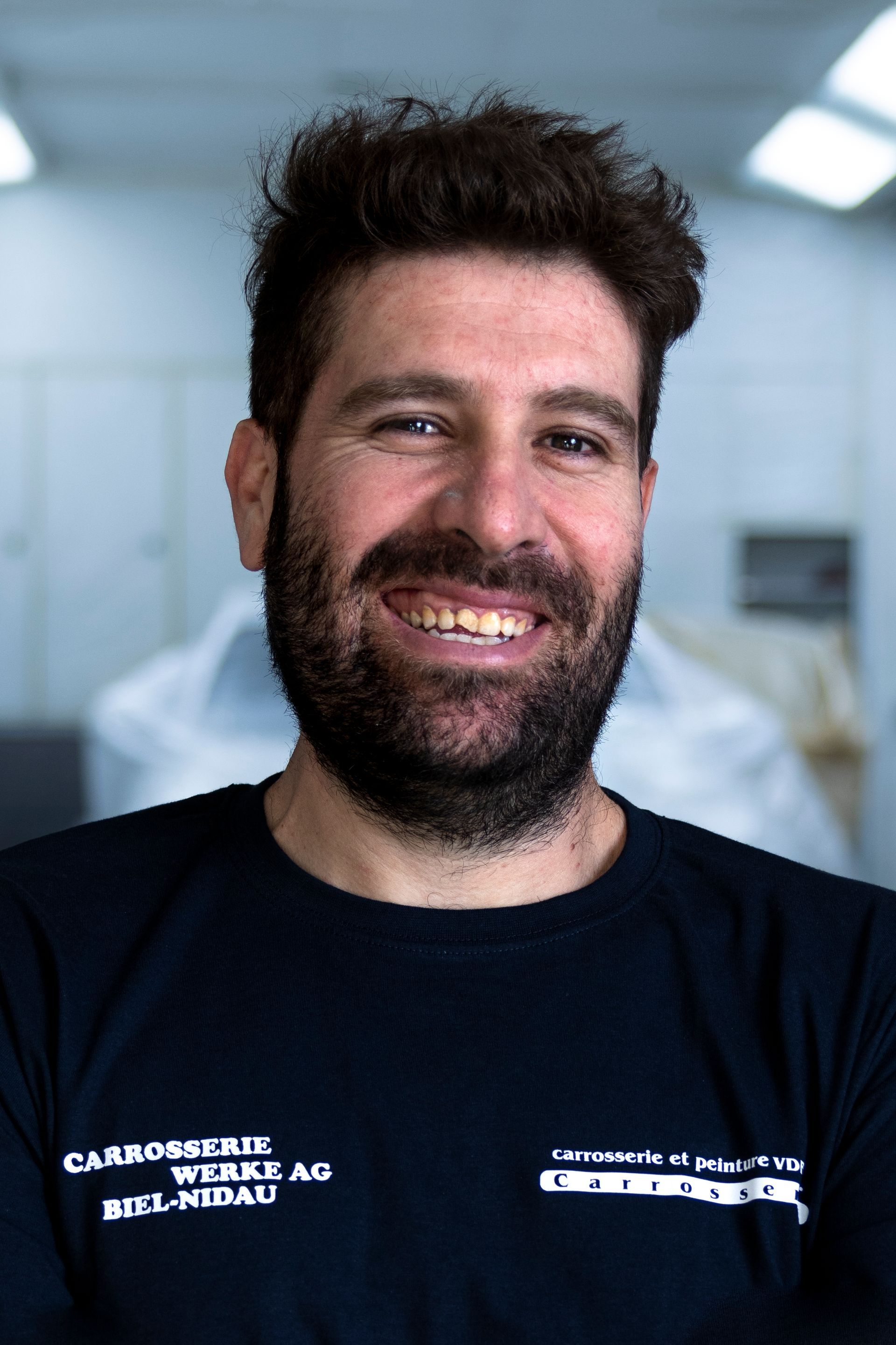 Frau mit kurzen braunen Haaren, lächelnd, mit weißem Blazer und Halskette, drinnen.