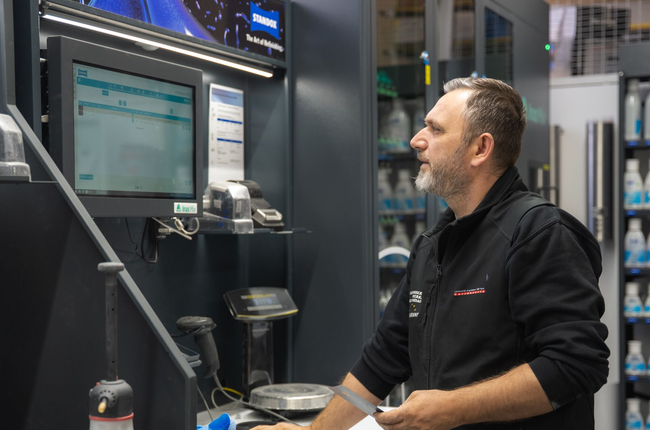 Eine Person im Schutzanzug bedient eine Maschine in einer sterilen Umgebung und ist an ein Beatmungsgerät angeschlossen.