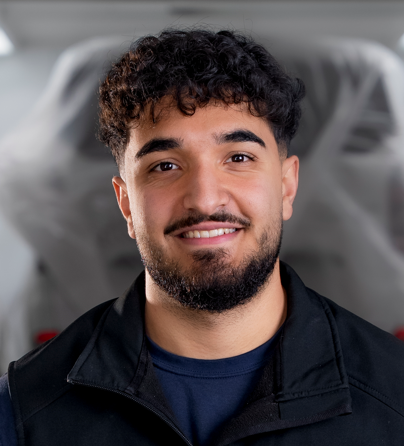 Mann mit ergrauendem Haar und Bart, lächelnd, trägt ein blaues Sweatshirt mit Text, drinnen.