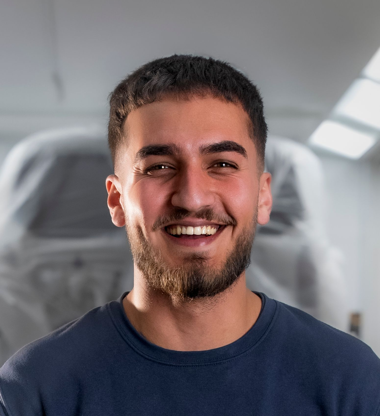 Ein Mann in einem dunkelblauen Hemd lächelt in einer Werkstatt in die Kamera.