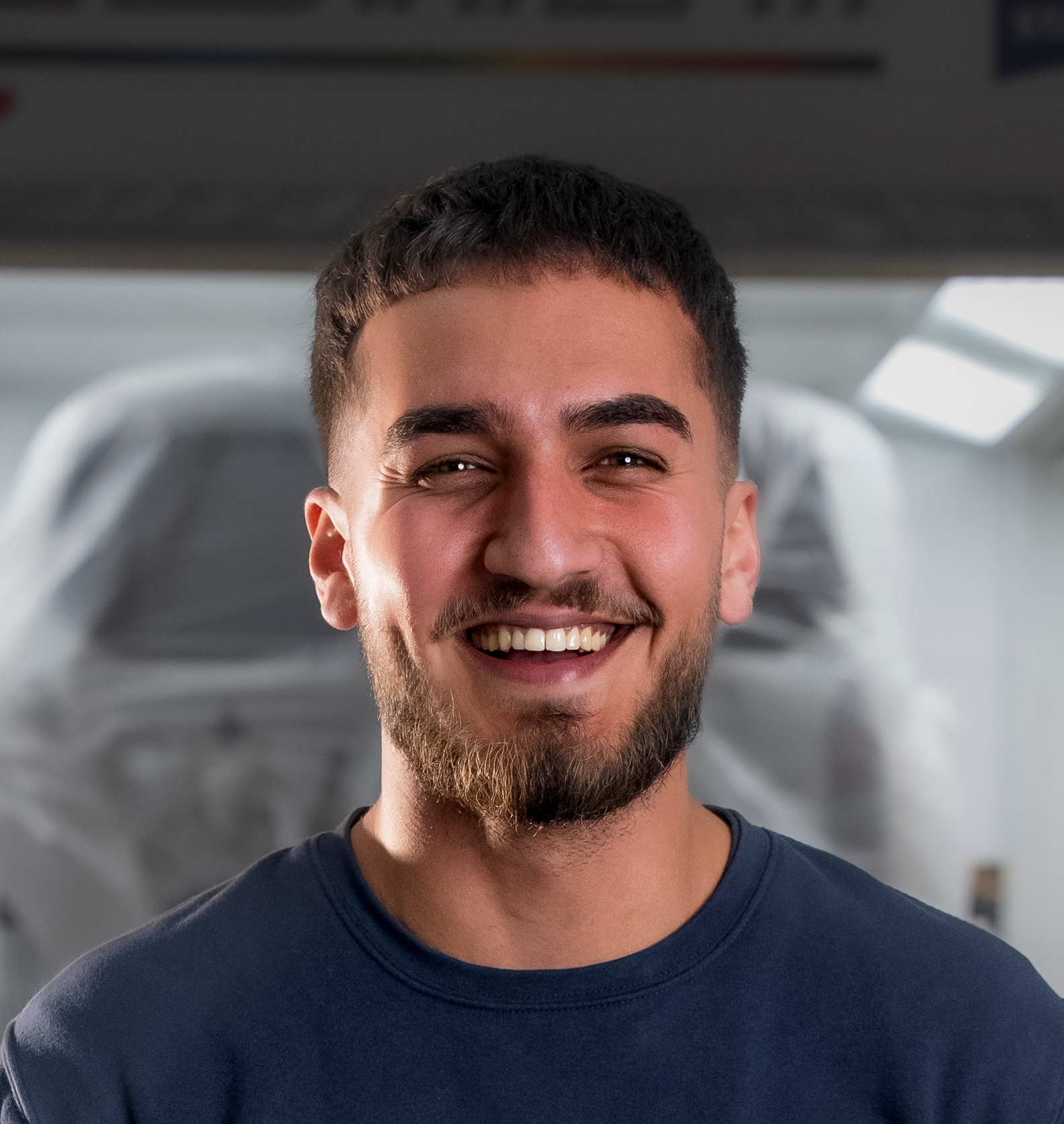 Ein Mann in einem dunkelblauen Hemd lächelt in einer Werkstatt in die Kamera.