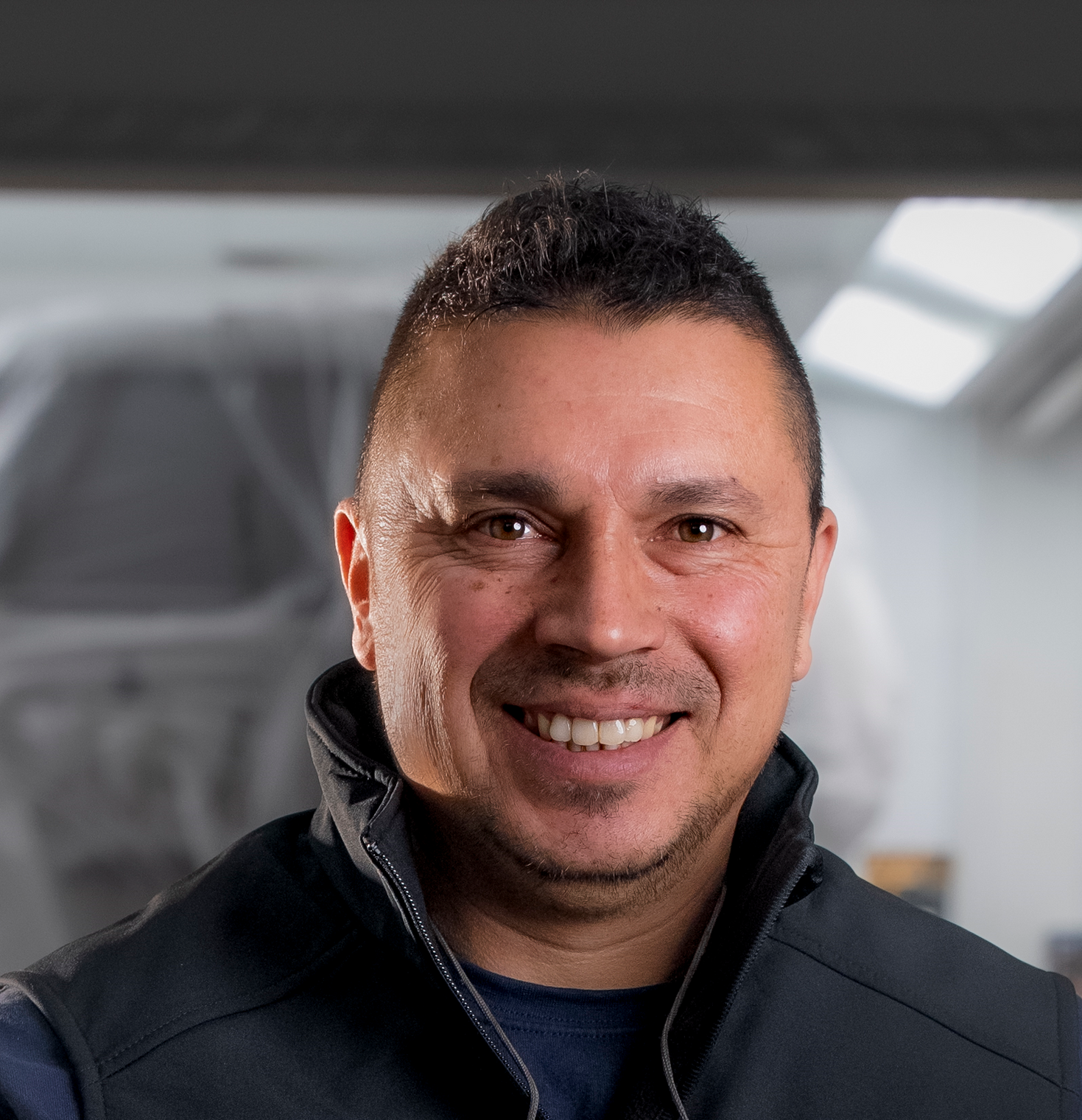 Frau mit kurzen braunen Haaren, lächelnd, mit weißem Blazer und Halskette, drinnen.