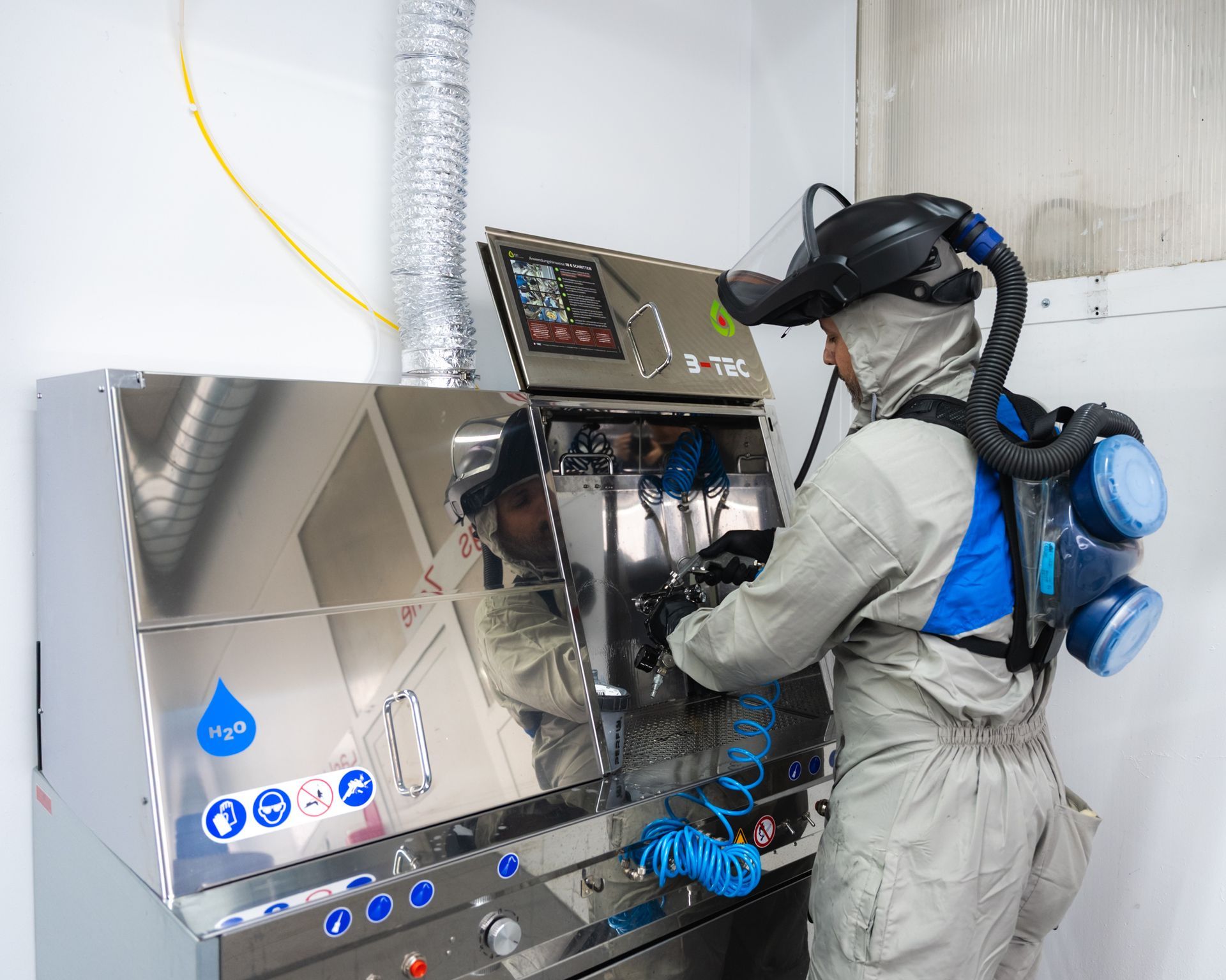 Eine Person im Schutzanzug bedient eine Maschine in einer sterilen Umgebung und ist an ein Beatmungsgerät angeschlossen.