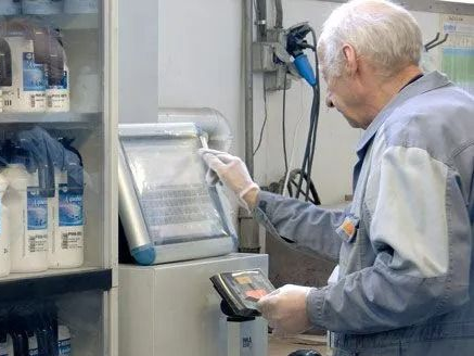 Eine Person im Schutzanzug bedient eine Maschine in einer sterilen Umgebung und ist an ein Beatmungsgerät angeschlossen.