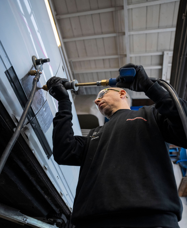 Eine Person im Schutzanzug bedient eine Maschine in einer sterilen Umgebung und ist an ein Beatmungsgerät angeschlossen.