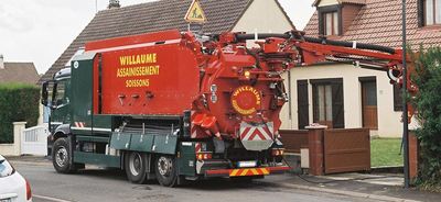Camion municipal rouge avec dévidoir de tuyau stationné à côté de maisons dans une rue résidentielle.