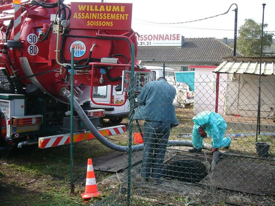 Des ouvriers nettoient une plaque d'égout à côté d'un camion-citerne rouge de Willaume Assainissement.