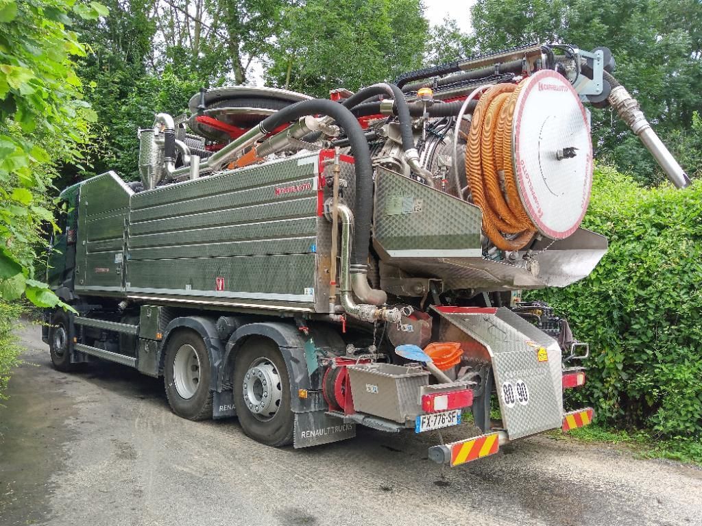 Un gros camion utilitaire, équipé de tuyaux et de matériel, est stationné sur une route boisée étroite.