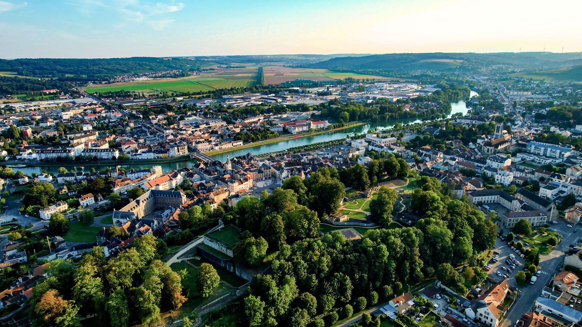 Vue aérienne d'une ville avec des maisons, des routes et des arbres verdoyants au coucher du soleil.