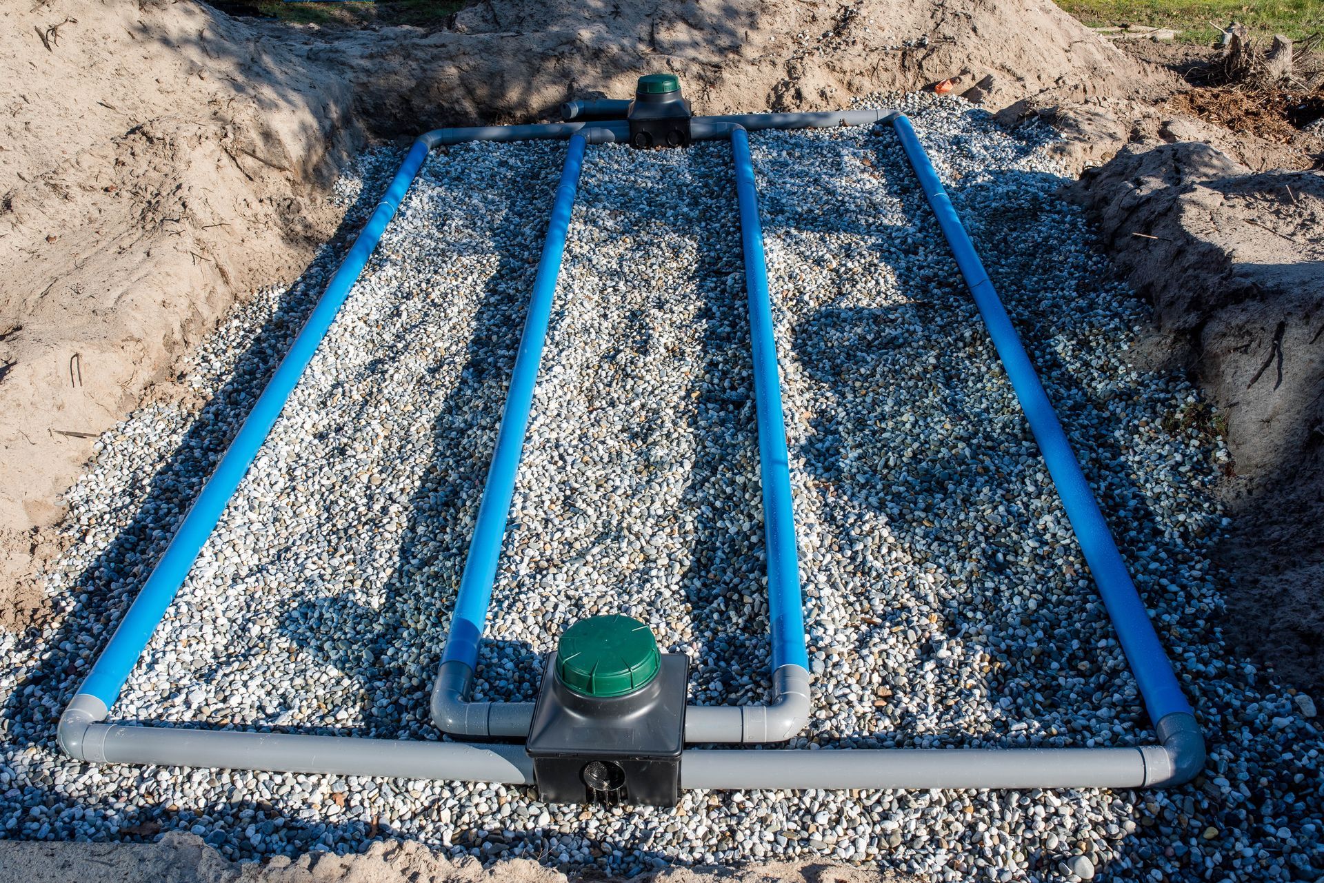 Fondation rectangulaire en gravier à cadre bleu, installée dans un chantier de fouilles, avec un petit chapeau vert au centre avant.