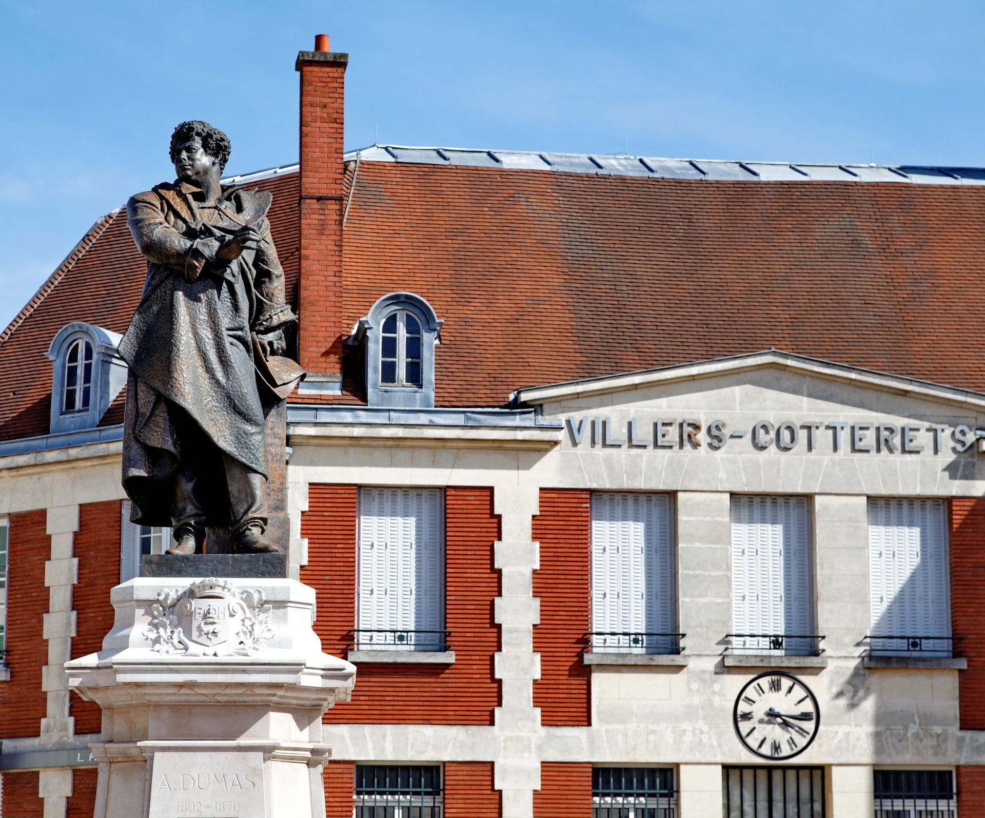 Statue devant l'hôtel de ville de Villers-Cotterêts avec horloge et bâtiment au toit rouge.