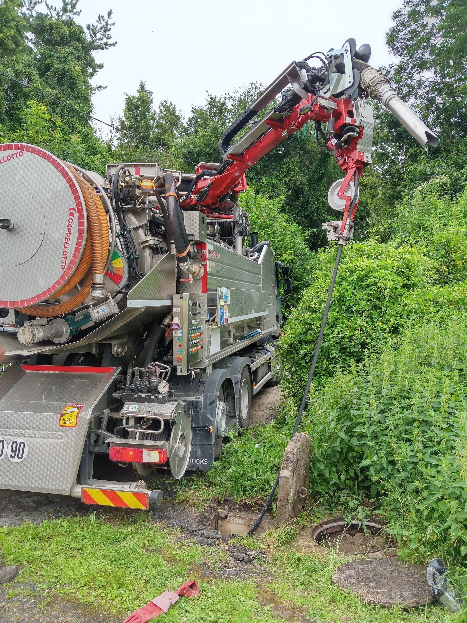 Machine hydraulique dans un épais fourré vert, soulevant un tronc d'arbre coupé avec son bras grappin rouge.