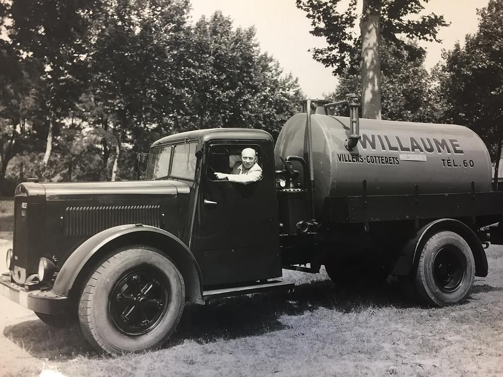 Camion-citerne noir vintage garé à l'extérieur avec des arbres en arrière-plan.