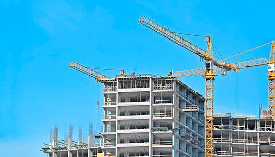 Se está construyendo un edificio con grúas y un cielo azul al fondo.
