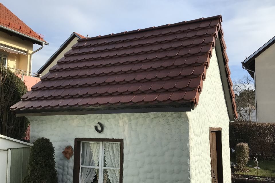 Kleines, weiß verputztes Gebäude mit braunem Ziegeldach. Es verfügt über ein Fenster und eine Tür.