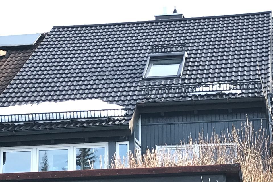 Dunkelgraues Ziegeldach mit Oberlicht, Schnee und eine dunkle Holzfassade.