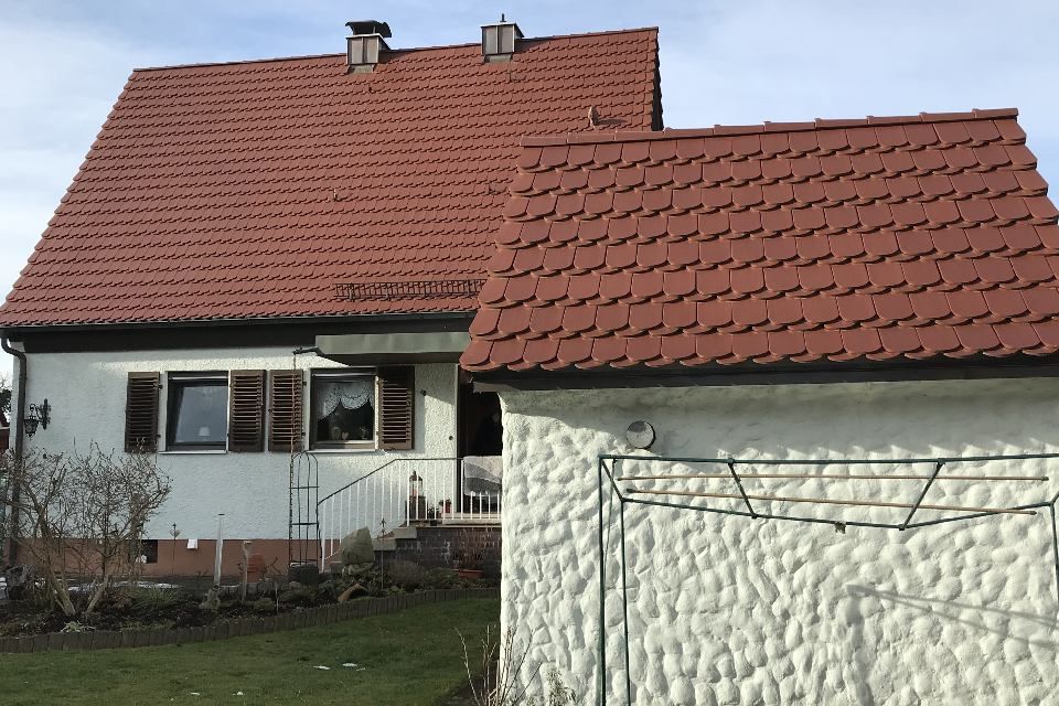 Weißes Haus mit rotem Ziegeldach, Fensterläden und einer kleinen Garage.