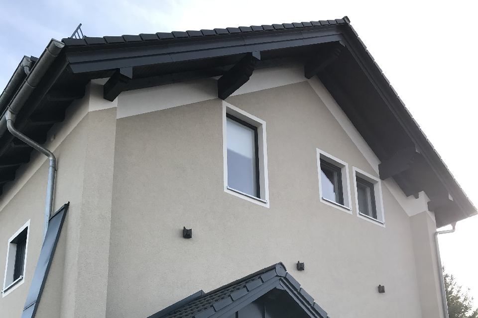 Beige Hausfassade mit schwarzen Zierelementen, Fenstern und Dach.