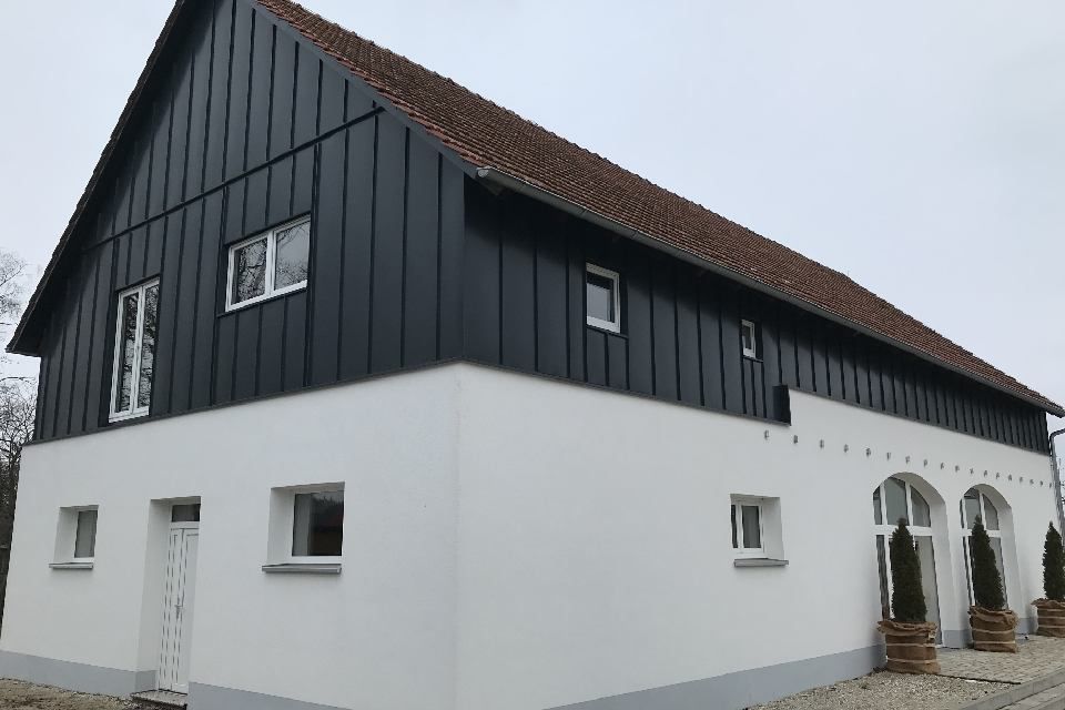 Weißwandiges Gebäude mit schwarzem Oberteil und rotem Ziegeldach.