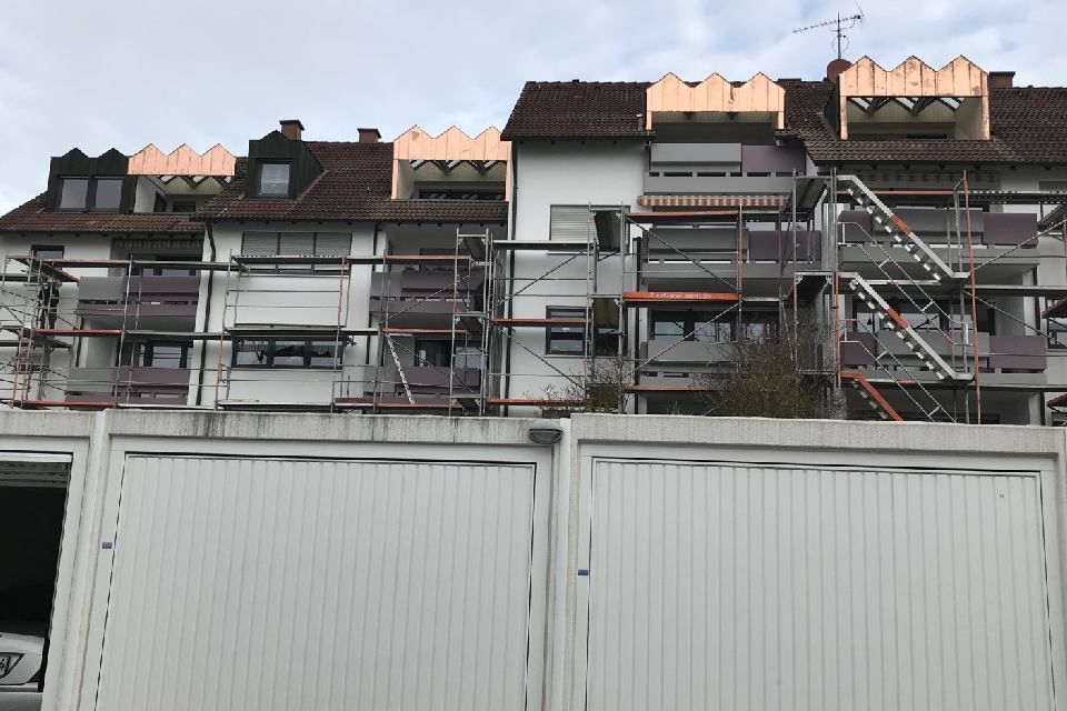 Wohnhaus mit Gerüsten, weißen Balkonen und Garagen im Vordergrund.