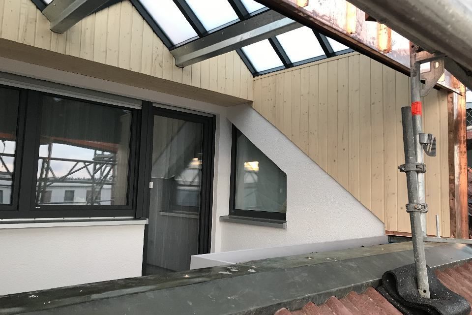 Außenansicht des Daches eines Gebäudes mit Fenstern, Holzverkleidung und Gerüst.