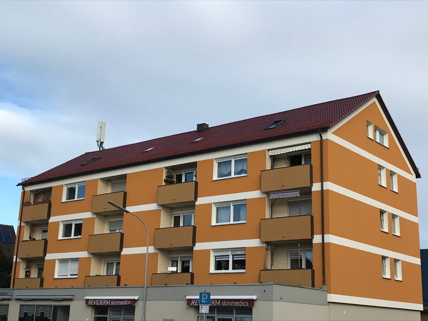 Orangefarbenes Wohnhaus mit rotem Dach, Balkonen und Fenstern; blauer Himmel im Hintergrund.